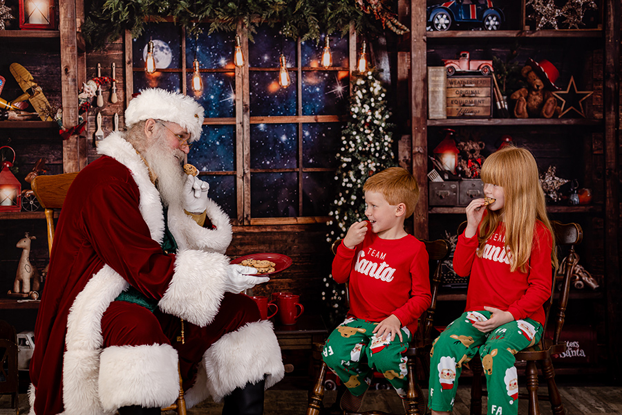 two children wearing a Team Santa pj shirts having cookies with Santa
